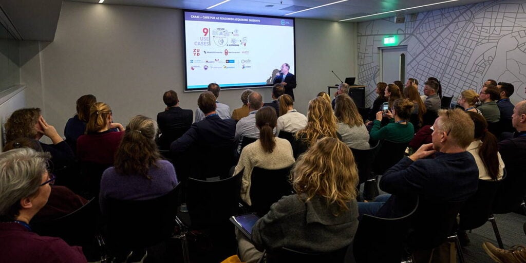 Conference attendees listening to a speaker presenting healthcare technology insights at the ICT&amp;health World Conference.