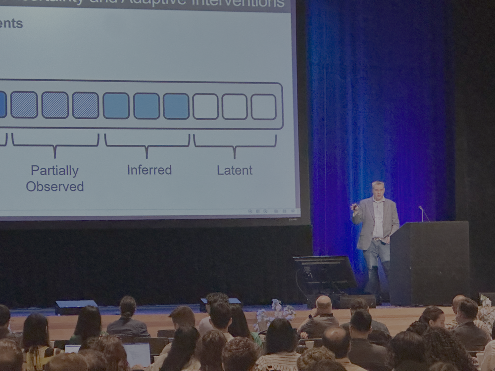 Speaker presenting machine learning and healthcare research findings to a conference audience on stage.